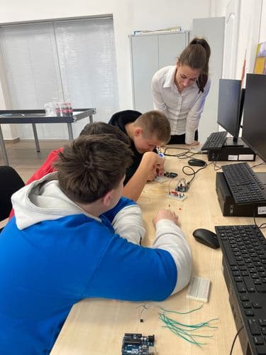 a DKA teremben (digitális közösségi alkotótér) három diák a számítógépek előtt ül és integrált áramköröket szerel, a háttérben egy tanárnő instruálja őket