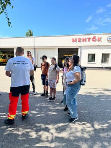 PO tábor 2024 - a váci mentőállomás kívülről, egy mentős háttal áll és magyaráz a körülötte álló tanulóknak