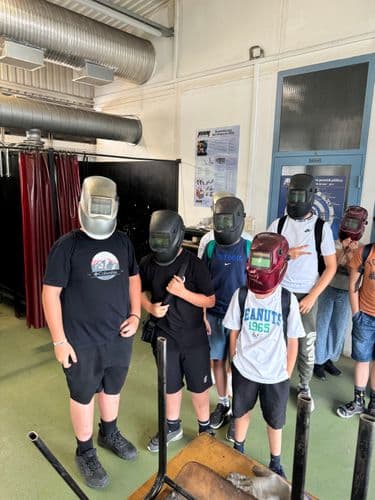  PO tábor 2024-  Tanulók egy műhelyben hegesztőpajzsot viselnek a fejükön, előttük egy asztal fémszerkezete, valószínűleg azon gyakoroltak