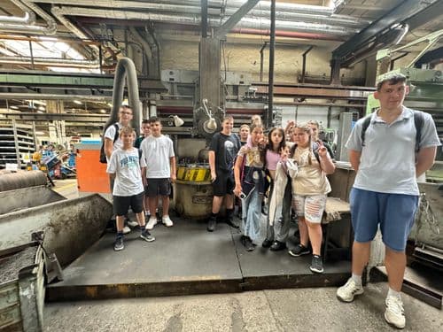 PO tábor 2024. tanulók csoportképe a BKV járműjavítóban különféle szervizes nagygépekkel a háttérben