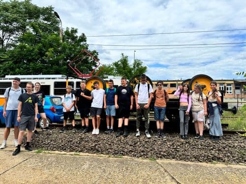 PO tábor 2024 - tanulók csoportképe a BKV telephelyén, egy sárga villamos előtt állnak