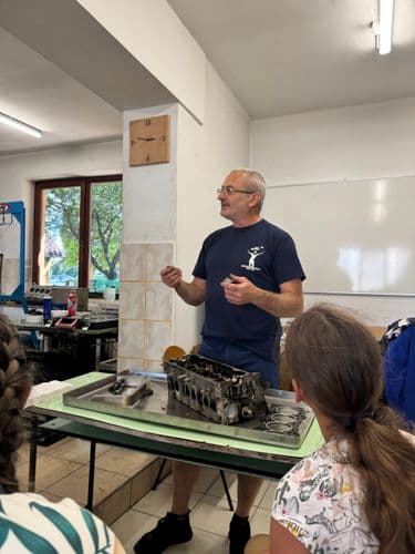 PO tábor 2024 - Autószerelő oktató egy asztalnál állva magyarázza az előtte fekvő szétszedett sebességváltó működését