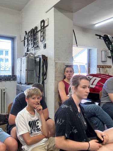 PO tábor 2024-  Három tanuló a vszc autószerelő műhelyében figyel az okatóra, a háttérben motorblokk tömítések, kapcsolótáblák a falakon