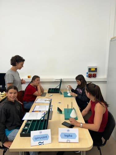 PO tábor 2024 logisztikai játékkal játszik öt tanuló, akik egy hosszú asztalnál ülnek a DKA teremben