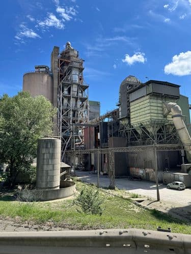 PO tábor 2024 - a Duna-dráva cement üzeme kívülről, szép felhős kék ég háttérrel. Cementtárolók, csövek és állványok látszanak, igazi ipari kép